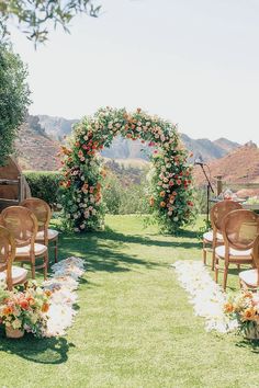 an outdoor ceremony set up with chairs, flowers and greenery on the grass in front of mountains