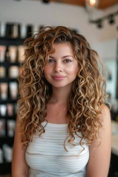 Woman with long curly hair wearing a white sleeveless top, smiling softly in a well-lit room with shelves of products in the background. Long Brown Hair With Highlights, Balayage Hair Copper