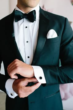 a man in a tuxedo with his hands on his lapel and wearing a black bow tie