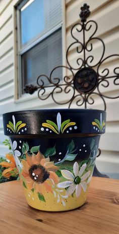 a painted flower pot sitting on top of a wooden table next to a metal planter