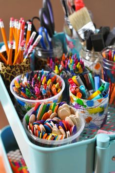 there are many pencils and crayons in cups on the table next to each other