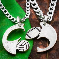 two silver necklaces with volleyball and basketball charms hanging from them on a green leaf