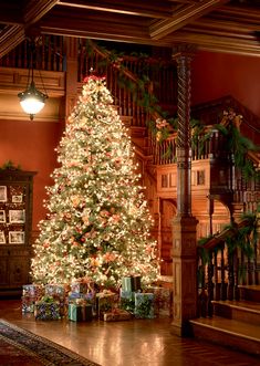 a decorated christmas tree in the middle of a living room with stairs and railings