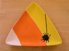 a yellow and orange plate with a black spider on the front, sitting on a wooden table