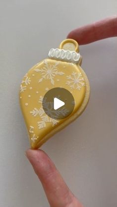 a hand holding a small yellow ornament with white snowflakes on it