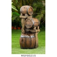 a water fountain made out of wooden barrels in the grass with palm trees behind it