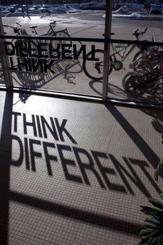 the shadows of bicycles are cast on the floor in front of a glass window that reads think different