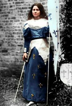 a woman dressed in medieval clothing holding a snowboard and skis next to a brick wall