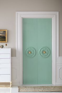 a white room with two green doors and a dresser in the corner next to it