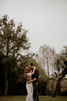 a bride and groom embracing in the middle of a field with palm trees behind them