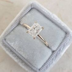 an engagement ring with a princess cut diamond in it on a velvet box that is sitting on a table