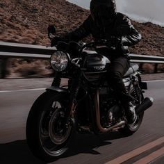 a man riding on the back of a motorcycle down a road next to a mountain