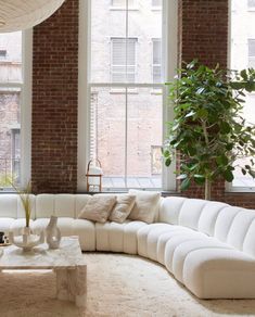 a large white couch sitting in front of a window next to a potted plant