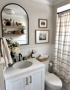 a white toilet sitting next to a sink in a bathroom under a mirror and framed pictures