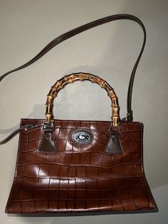 This vintage Dooney & Bourke purse features brown leather and unique bamboo handles and also be used with a shoulder strap. The satchel/top handle bag style is perfect for any occasion, and the spacious interior is lined with high-quality leather for a luxurious feel. With a focus on the brand, department, style, and material aspects, this purse is a must-have for any fashion-forward woman. The exterior color is a classic brown that will never go out of style, and the exterior material is durable leather that will last for years to come. Add this beautiful bag to your collection today. Made in USA Vintage Dooney And Bourke, Classic Brown, Bamboo Handles, Dooney And Bourke, Bag Style, Dooney & Bourke, Handle Bag, Beautiful Bags, High Quality Leather