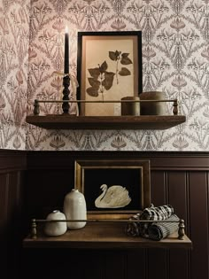 a shelf with some pictures and candles on it in front of a wallpapered wall