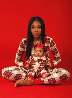 a woman sitting on the floor holding a baby in her lap and wearing plaid pajamas