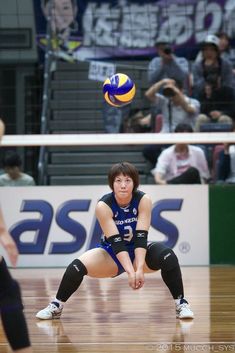 a volleyball player squatting down to catch the ball in front of her and people watching