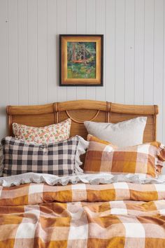 a bed with plaid sheets and pillows in a small room next to a painting on the wall