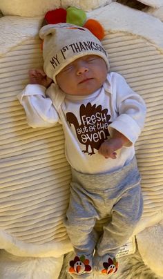 a baby laying on top of a bed wearing a thanksgiving shirt and pants with a turkey hat