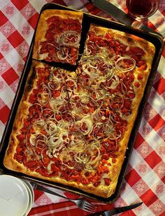 a pizza sitting on top of a red and white checkered table cloth next to a glass of wine