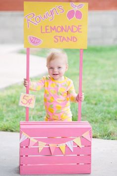 a baby in a pink lemonade stand with a sign that says rowan's lemonade stand