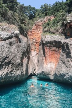 two people swimming in the water near large rocks