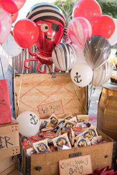 a trunk filled with candy and balloons on top of a wooden table next to other items