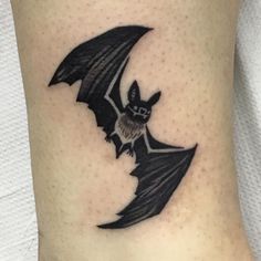 a small bat tattoo on the side of a woman's leg, it is black and white