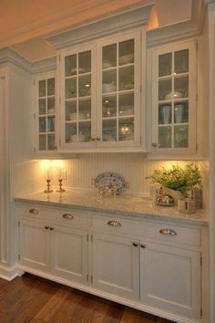 a kitchen with white cabinets and wood flooring in the center is lit by two lights