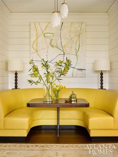 a yellow couch sitting in front of a painting on the wall next to a table