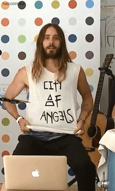 a man sitting in front of a laptop computer holding a sign that says city af angels