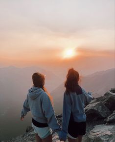 two girls standing on top of a mountain looking at the sunset