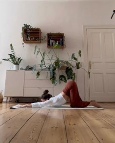 a woman is doing yoga on the floor in front of a potted plant and bookshelf