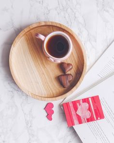 a cup of coffee and some chocolates on a wooden plate next to an open book