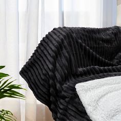 a black and white blanket sitting on top of a bed next to a potted plant