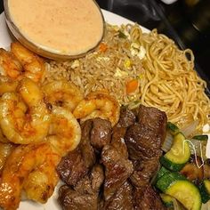 a plate full of food with shrimp, noodles and sauce on the side at a restaurant