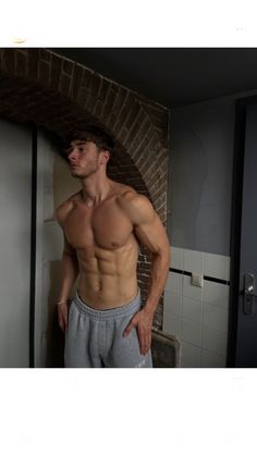 a shirtless man standing in front of a brick wall with his hands on his hips