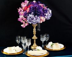 purple and pink flowers are in a gold vase on a blue table cloth with wine glasses