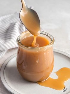 a spoon pouring caramel sauce into a glass jar on a plate with a white towel