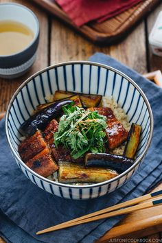 a bowl filled with meat and vegetables next to chopsticks on top of a wooden table