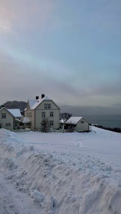 a snow covered road with houses and mountains in the background on a cloudy day at dusk