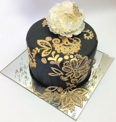 a black and gold decorated cake sitting on top of a silver plate with a white flower