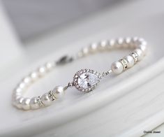 "These dainty yet elegant bracelet is created with a cubic zirconia teardrop and Austrian pearls in ivory/cream.  Pearls measure 6 mm and are accented with rhinestone rondeles for extra sparkle!  Bracelet measures approximately 7 1/2\" long. Focal measures just over  1/2\" long by just under 1/2\" wide.  Please leave your actual wrist measure at checkout to ensure proper fit.  This bracelet is a great gift idea for bridesmaids, mother of the bride, mother of the groom, maid of honor, someone special, or just to spoil your self.  It comes in a white gift box with black ribbon ready to give. This bracelet is created to complement the Audrey collection. Please choose desired pearl color at checkout.      If your dress is ivory I recommend the white color this is an off white and works with wh Classic Pear-shaped Bracelets For Wedding, Pear-shaped Silver Bracelet For Weddings, Elegant Pear-shaped Bracelets For Wedding, Elegant Pear-shaped Bracelet For Wedding, Silver Teardrop Bracelet For Wedding, Bridal Pearl Bracelet, Bridal Bracelet Pearl, Sparkle Bracelet, Pearl Cuff