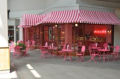 an outdoor cafe with pink chairs and striped awnings on the front entrance to it