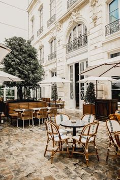 tables and chairs with umbrellas in front of a large building on a cobblestone street