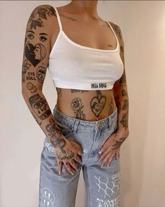 a woman with many tattoos on her body and hands behind her back, standing in front of a white wall