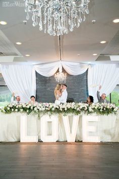 a bride and groom kissing in front of the love sign at their wedding reception table