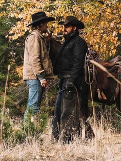 two men in cowboy hats standing next to each other with a horse behind them on a field