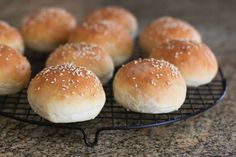 small buns with sesame seeds on a black wire rack sitting on a granite countertop